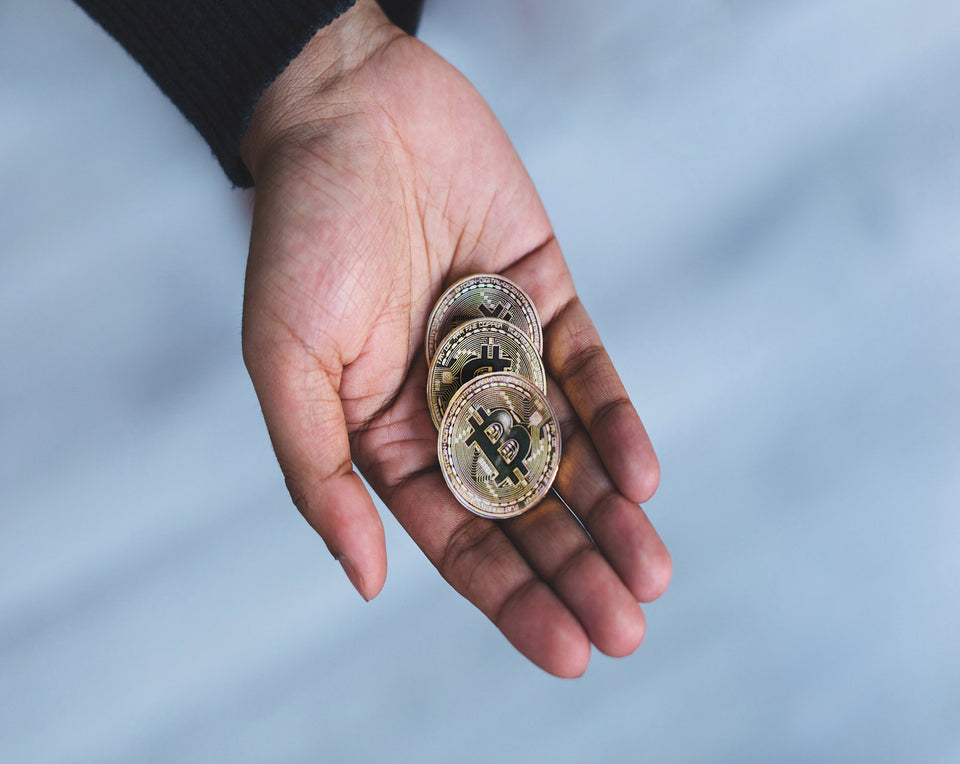A person holds a handful of bitcoin cryptocurency.  The person is wearing a black, long sleeve shirt. 